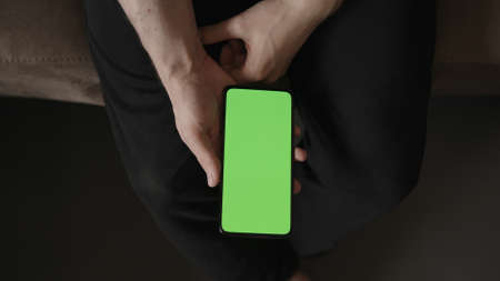 POV top view shot of man show phone with green screen indoor sitting on a couch