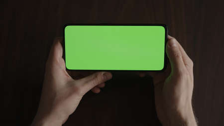 Man using phone with green screen on black wwalnut table