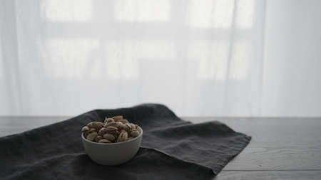 salted pistachios from white bowl on oak tableの写真素材