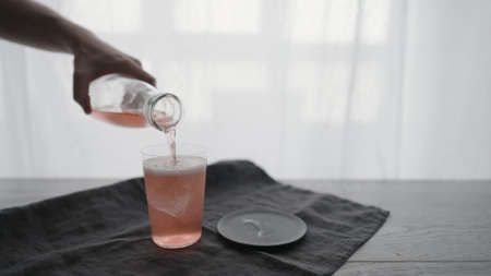 Man pour pink sparkling drink into tumbler glass with ice chunkの写真素材