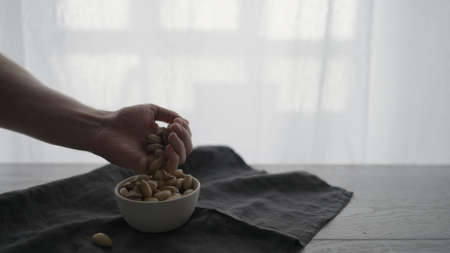 Man pick salted pistachios from white bowl on oak tableの写真素材