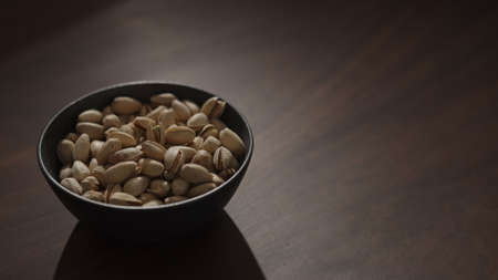 roasted pistachios in black bowl on walnut table