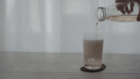 pour rose drink into tumbler glass on white tableの写真素材