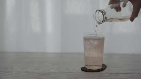 pour rose drink into tumbler glass on white tableの写真素材