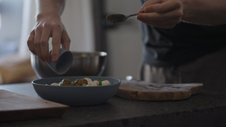 Man pour dressing into salad with mixed green, tomatoes and mozzarella on concrete countertopの写真素材