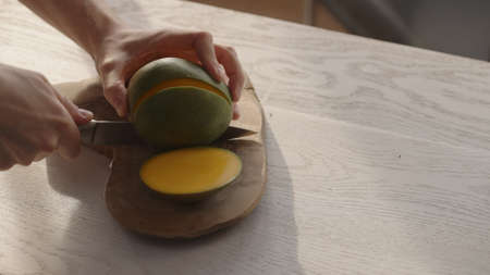 Man cutting ripe mango on olive board on white oak tableの写真素材