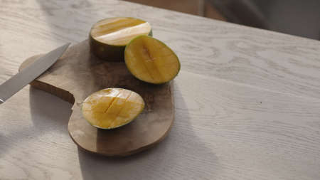 Ripe mango on olive board with knife on white oak tableの写真素材