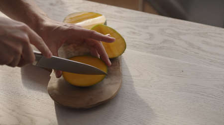 Man cutting ripe mango on olive board on white oak tableの写真素材