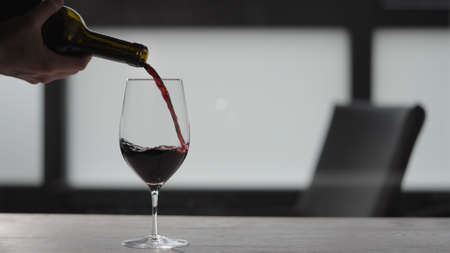 Pour red wine into wineglass on white oak table with copy spaceの写真素材