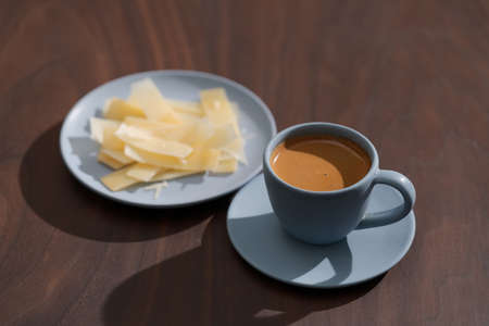 Fresh espresso in blue cup with cheese flakes on walnut table