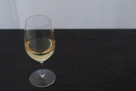 White wine in a wineglass on black oak table with copy space, shallow focusの写真素材