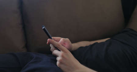 Closeup young man use smartphone working from home lying on couch side view