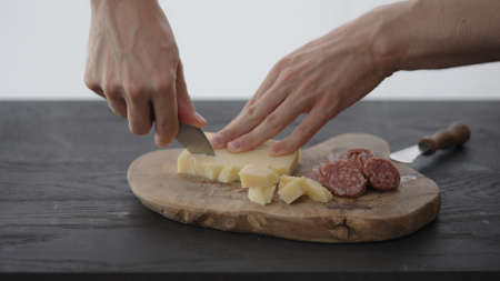 Man cuts some vintage cheese next to cured sausage on olive board with copy spaceの写真素材