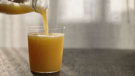 pour orange juice in tumbler glass on oak table with copy spaceの写真素材