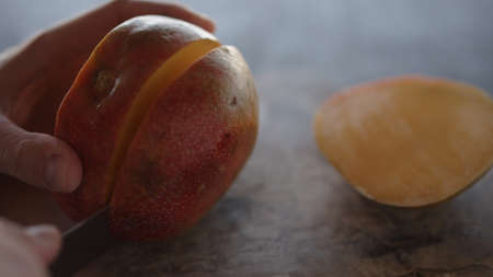 Man cut ripe big mango on olive wood board