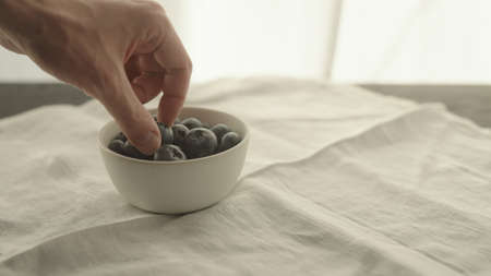 man put fresh blueberries in white bowl on linen napkinの写真素材