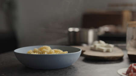 steam rising from boiled fusilli in blue bowl on concrete countertopの写真素材