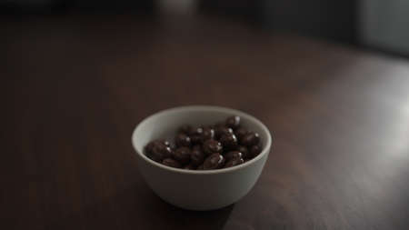 chocolate covered pistachios from white bowl on walnut table