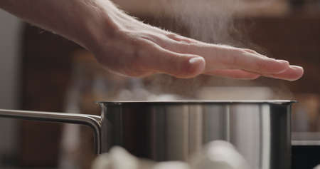 man handcheck temperature of steam rising from saucepan with boiling water on stoveの写真素材
