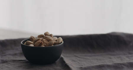 salted pistachios in black bowl on linen clothの写真素材