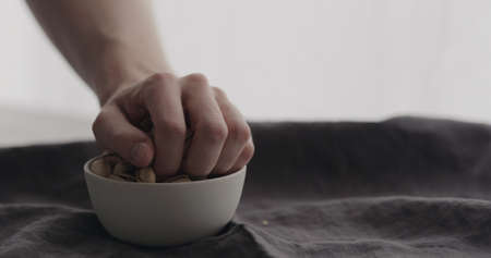 man hand take salted pistachios from white bowl on linen clothの写真素材