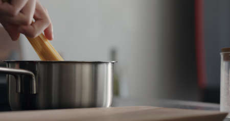 man hand put dried long fettuccine into saucepan with boiling waterの写真素材