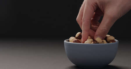 man hand take roasted hazelnuts from blue bowl on black backgroundの写真素材