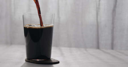 pour root beer into tumbler glass on oak table with copy spaceの写真素材