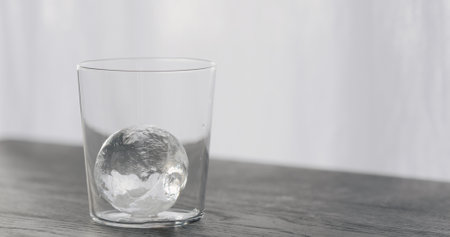 clear ice ball in tumbler glass on black oak tableの写真素材