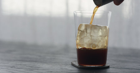 coffee pour over ice cube in tumbler glass on black wood tableの写真素材