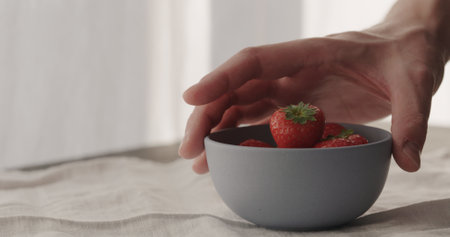 man put fresh strawberries in blue bowl on linen clothの写真素材