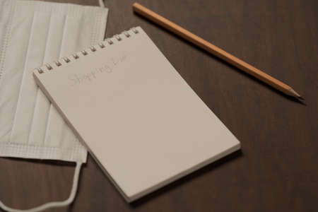 Notepad with shopping list on walnut table with protective mask and pencilの写真素材