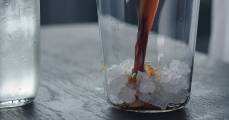 making espresso tonic, add crushed ice in tumbler glass and pour espresso on black wood tableの写真素材