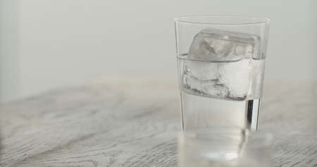 clear ice cube in tumbler glass with tonic on black oak table