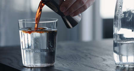 man pour syrup into tonic water with clear ice ball in tumbler glass on black oak tableの写真素材