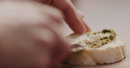 spread pesto on fresh baguette slice to make sandwich closeupの写真素材