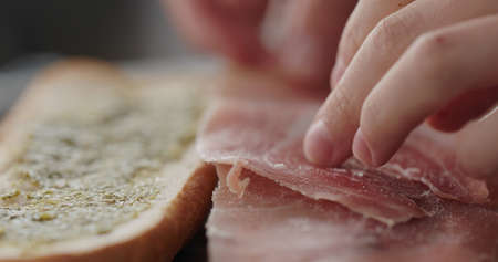 man put prosciutto slices on baguette to make sandwichの写真素材