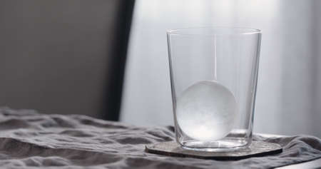 clear ice ball in tumbler glass on walnut tableの写真素材