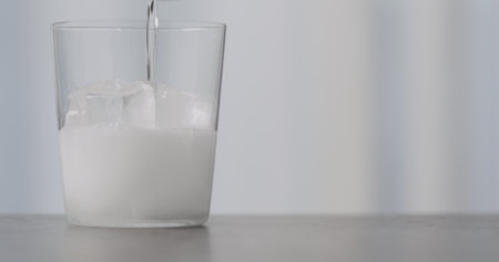 pour clear soda or tonic into tumbler glass with ice on concrete countertop with copy spaceの写真素材