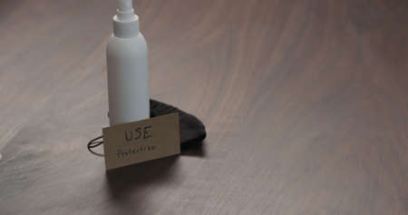 sanitizer white spray bottle on walnut wood table with black maskの写真素材
