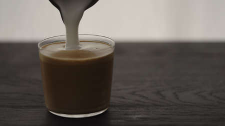 Pour steamed milk into espresso in tumbler glass on oak table with copy spaceの写真素材