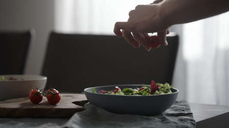 Making salad with cherry tomatoes and mixed greens in blue bowl on wood tableの写真素材