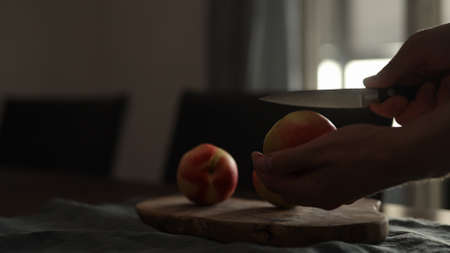 man cutting ripe nectarines on olive board in early morning