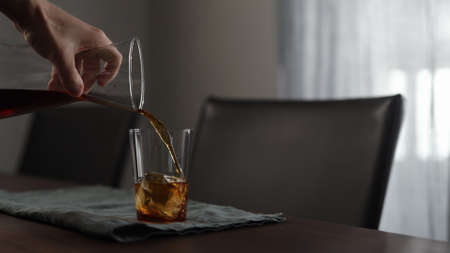 man pours fresh coffee over ice rock in tumbler glass on wood tableの写真素材