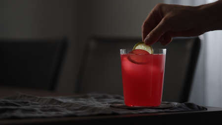 man decorating pink soft drink with lime slice in tumbler glass on tableの写真素材