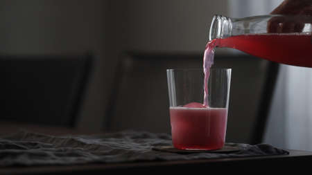 man pour pink soft drink over clear ice ball in tumbler glass on table