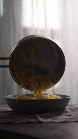 boiled hot fusilli pour in blue bowl with natural lightの写真素材