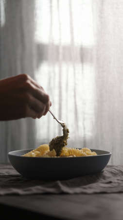 add pesto to boiled hot fusilli in blue bowl with natural light