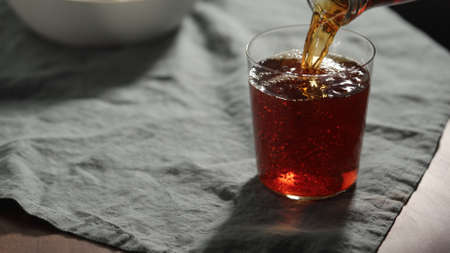 pour chinotto soft drink in tumbler glass on linen cloth