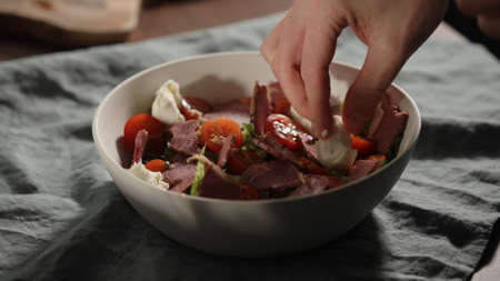 man add mozzarella, making salad in white bowlの写真素材